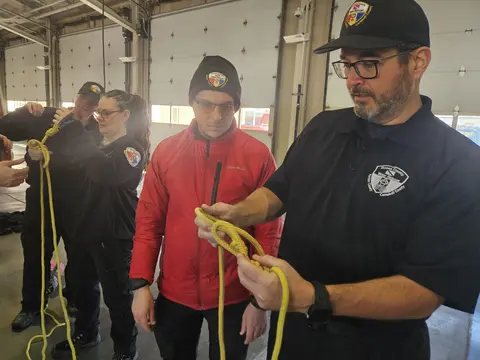 Team members conducting hands-on knot-tying and rope rigging training at a partner station.