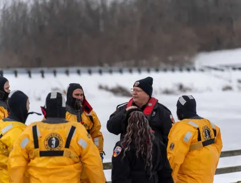 Team members standing on a snow-covered shore during winter ice rescue training.