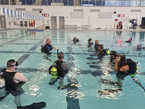 Public safety divers receiving poolside instruction before an underwater training session.
