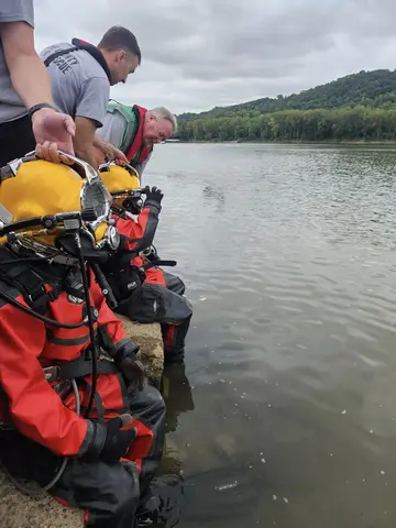 Crew members assisting public safety divers wearing Kirby Morgan underwater diving helmets.